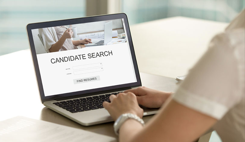 Image of a woman working on a laptop doing a candidate search for resumes with an online portal